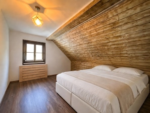 Un dormitorio con techo inclinado, una ventana, un banco de madera y una cama con ropa blanca.