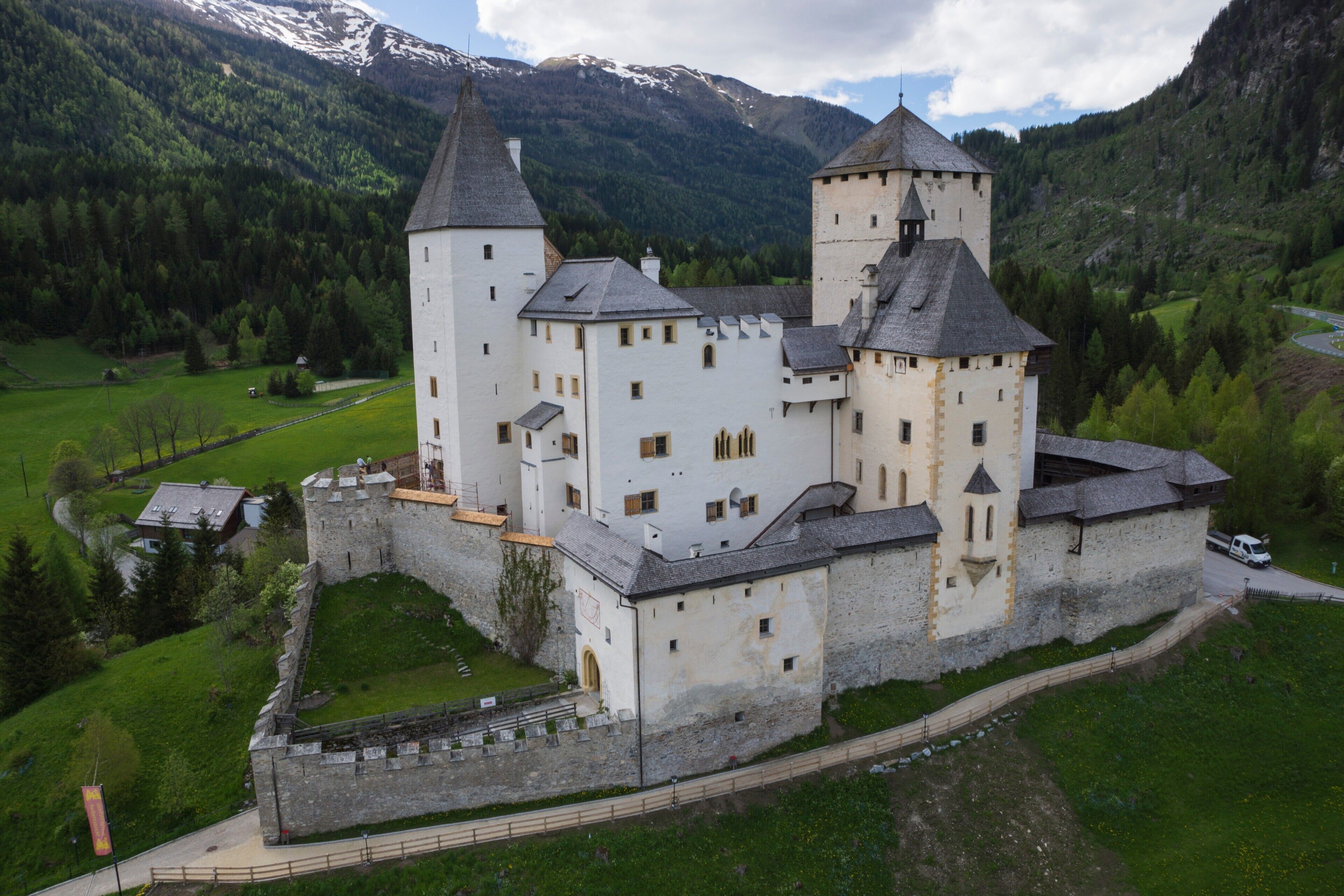 Un castillo con múltiples torres, rodeado por un foso y situado en un paisaje montañoso.