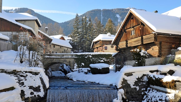 Un pueblo cubierto de nieve con edificios de madera, un puente de piedra y un río serpenteante.