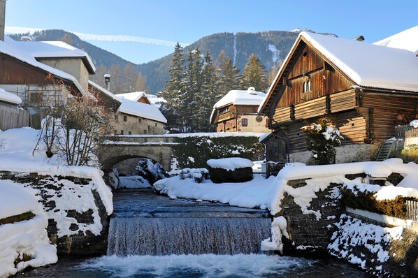 Un pueblo cubierto de nieve con edificios de madera, un puente de piedra y un río serpenteante.
