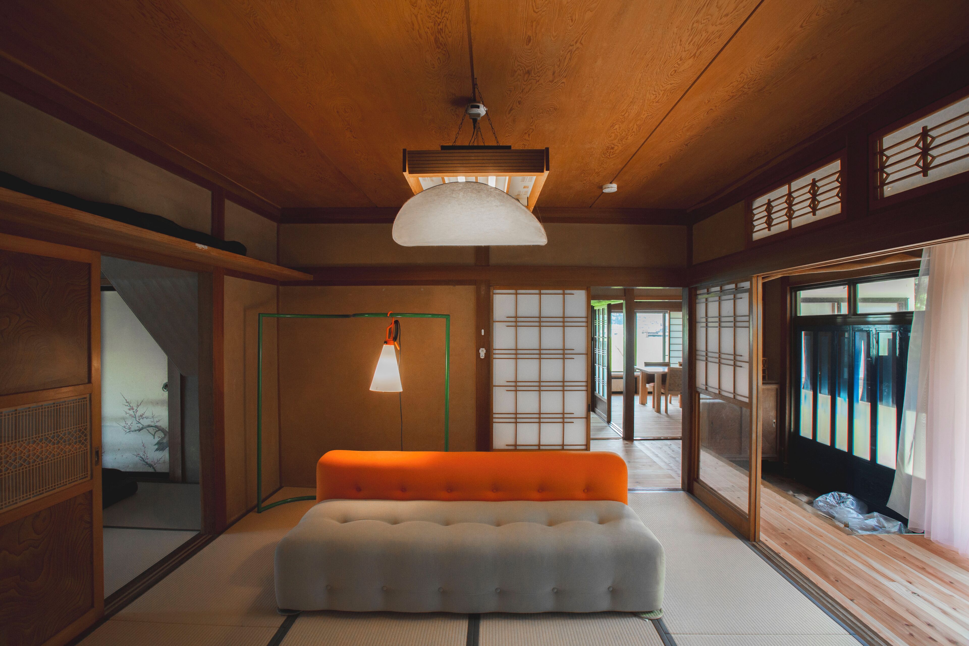 Una tradizionale stanza giapponese con pavimento in tatami, un divano basso color arancio e porte scorrevoli.