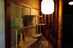 A wooden interior with shelves holding books and a bottle, a hanging light fixture, and a door. - NEO-Japanese House with Sauna in Rice Fields | Pet-Friendly·Workspace·Kitchen (佐久市)