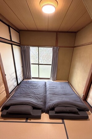 Een kamer met een traditioneel Japans interieur, met tatami vloerbedekking, shoji schermen en een futon bed.