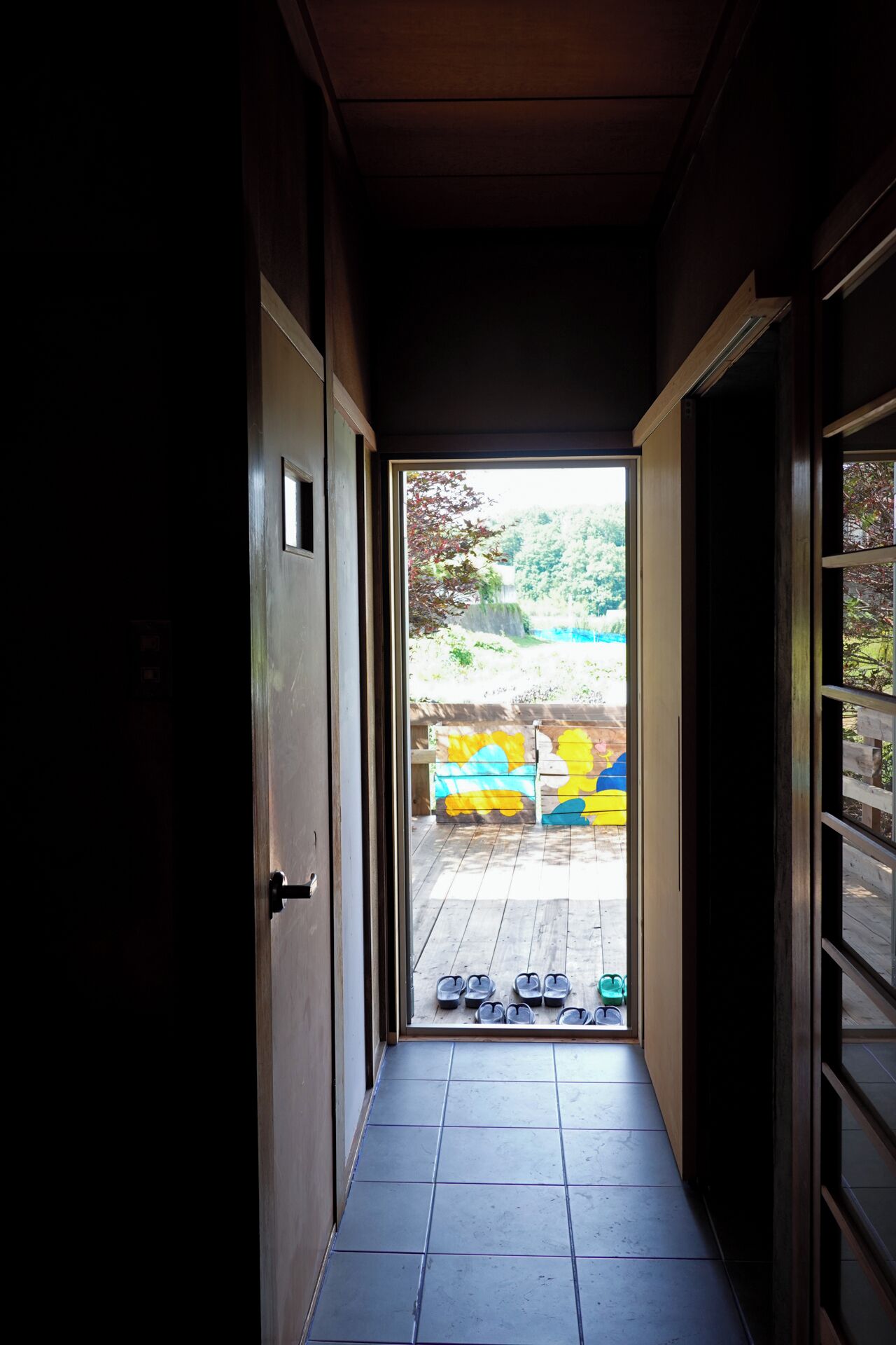 A narrow hallway leading to an outdoor area with a wooden deck and colorful painted blocks.