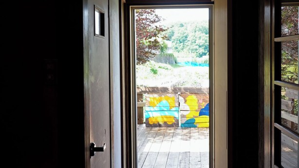 A narrow hallway leading to an outdoor area with a wooden deck and colorful painted blocks.