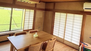A room with a wooden table and chairs, large windows with a view of greenery, and a ceiling fan. - NEO-Japanese House with Sauna in Rice Fields | Pet-Friendly·Workspace·Kitchen (佐久市)
