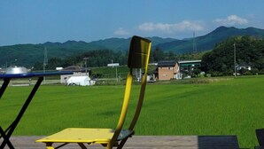 A deck with a yellow chair and a blue chair, overlooking a green field and distant hills.