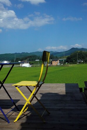 A deck with a yellow chair and a blue chair, overlooking a green field and distant hills.
