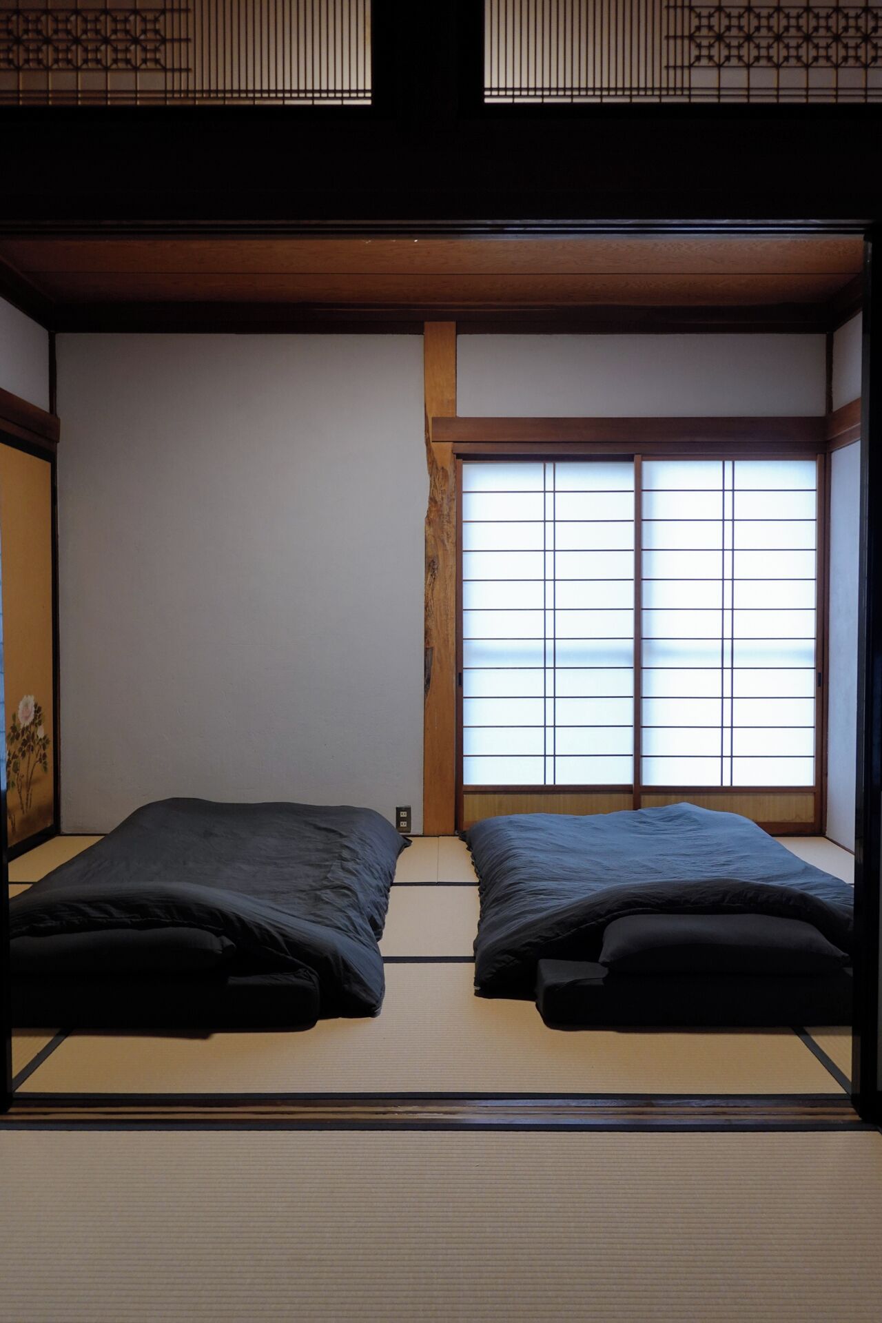 A traditional Japanese room with tatami flooring, a shoji screen window, and a low ceiling.