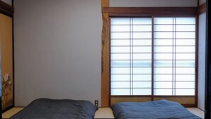 A traditional Japanese room with tatami flooring, a shoji screen window, and a low ceiling.