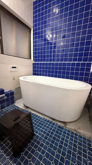 Een badkamer met een witte badkuip, blauwe betegelde wanden en een witte tegelvloer.