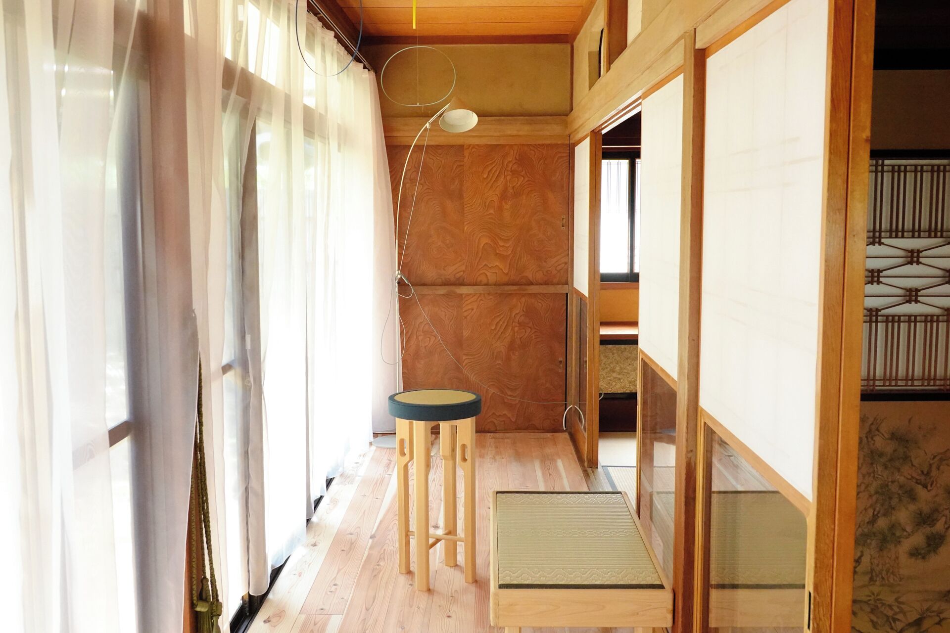 Un couloir étroit au plancher en bois, avec un petit tabouret, une table et un luminaire suspendu.