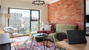 A modern living room with a large window, a brick wall, and a laptop on a table. - Wintera Residence - River View Apartment (Gdańsk)
