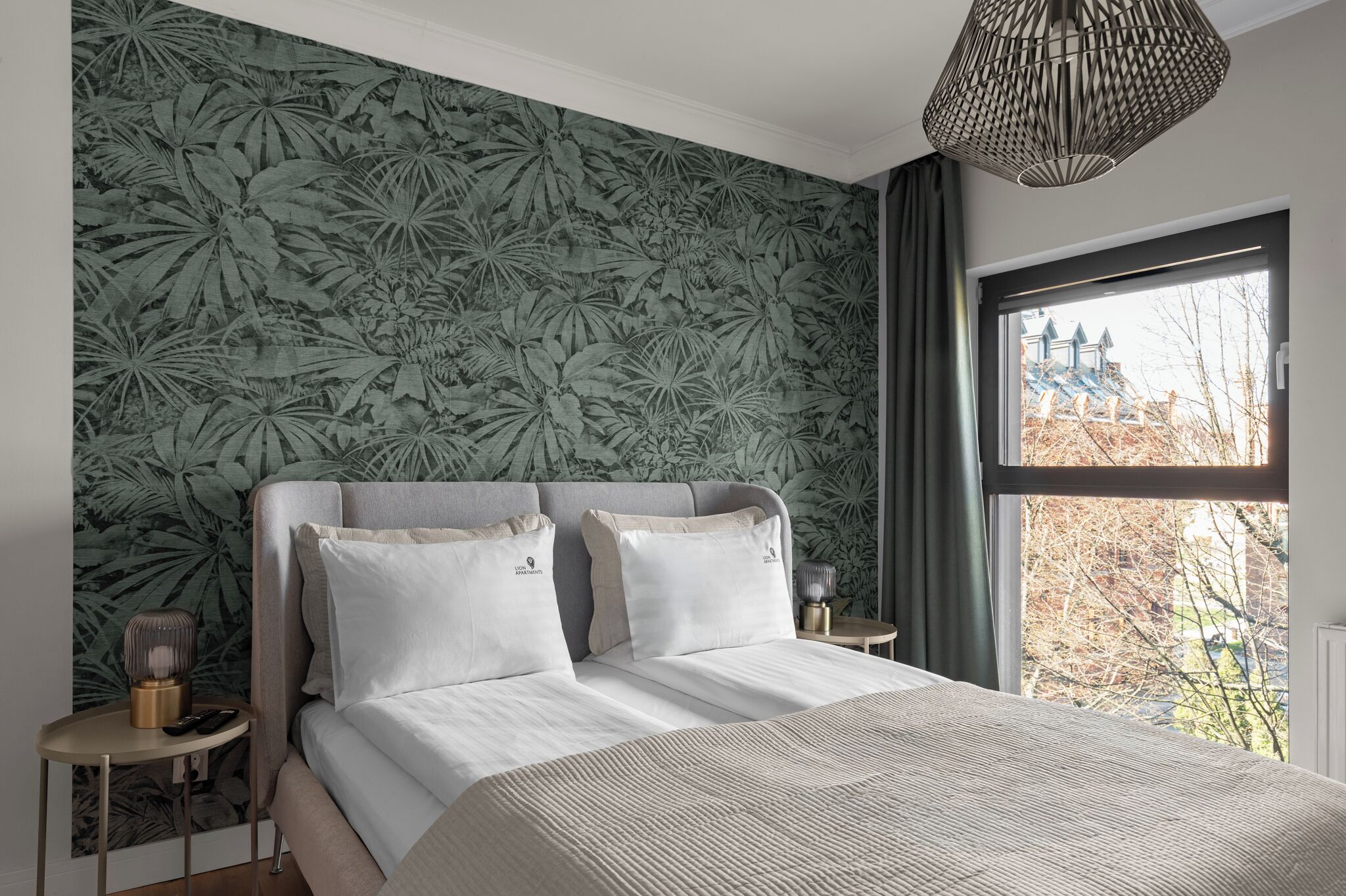 Een slaapkamer met een groot bed, een nachtkastje, een lamp en een raam met uitzicht op bomen.