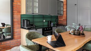 A modern kitchen with a coffee machine, a laptop on a table, and green chairs. - Wintera Residence - River View Apartment (Gdańsk)