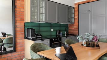 A modern kitchen with a coffee machine, a laptop on a table, and green chairs.