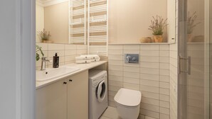 A modern bathroom with a built-in washing machine, a toilet, and a shower area. - Wintera Residence - River View Apartment (Gdańsk)