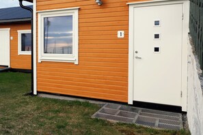 Ein eingeschossiges Gebäude mit weißer Tür und Fenster, einer kleinen Veranda und einem Schild mit der Nummer 1.