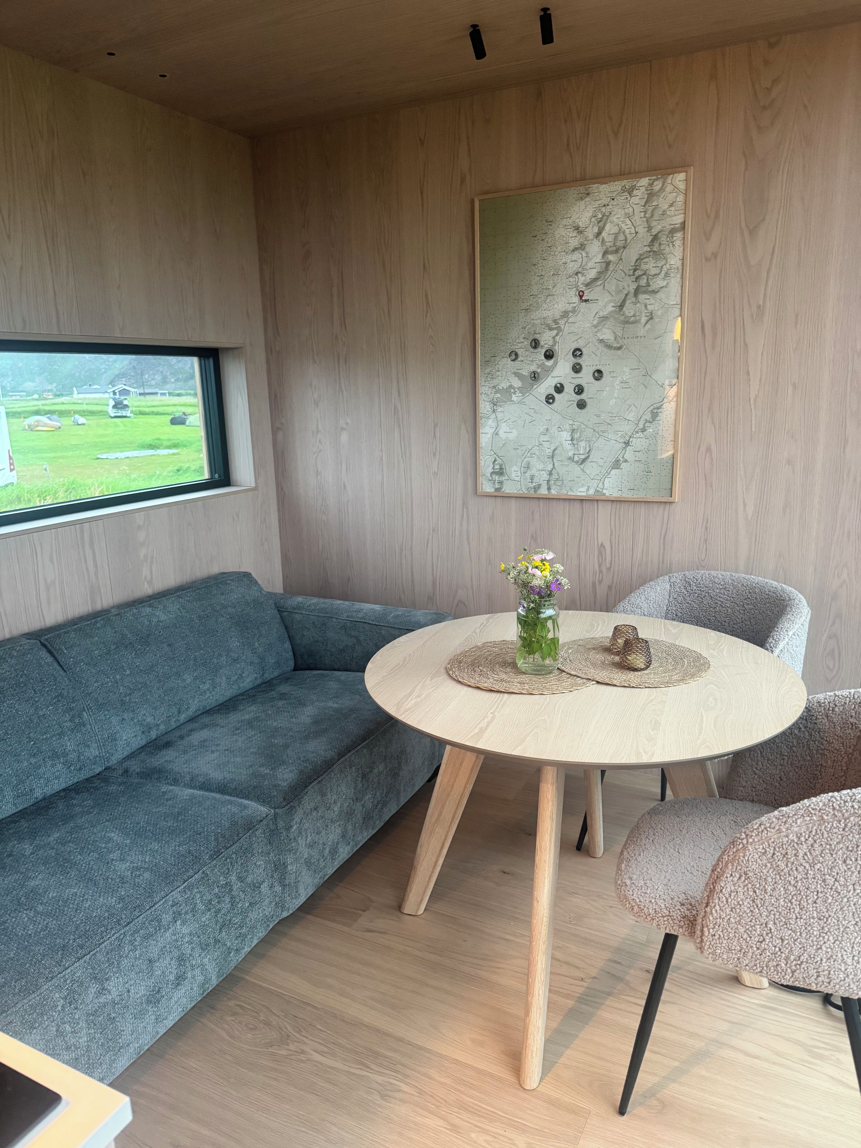 Un salón moderno con un sofá azul, una mesa redonda de madera con un florero y un mapa en la pared.