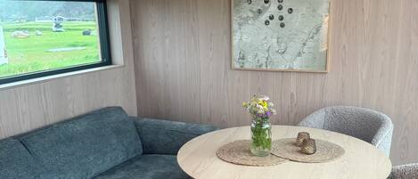A modern living room with a blue sofa, a round wooden table with a vase of flowers, and a map on the wall.
