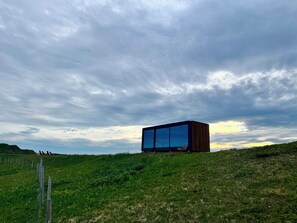 Un edificio moderno y minimalista con amplios ventanales de vidrio, ubicado en una colina cubierta de hierba bajo un cielo nublado.
