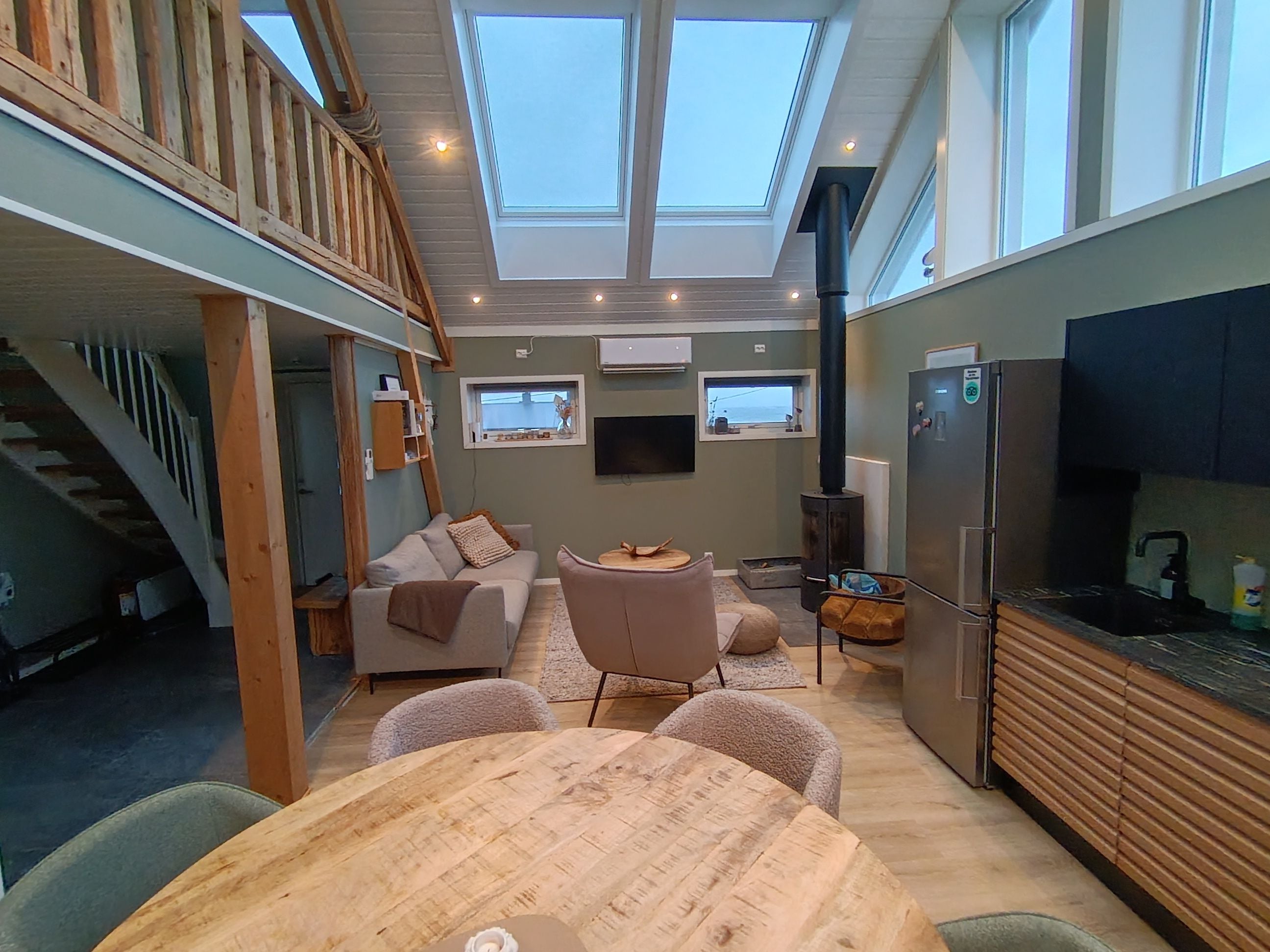 Un interior moderno con comedor, cocina y un espacio tipo loft con escalera de madera.