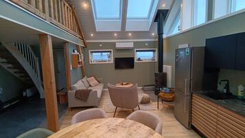 Un interior moderno con comedor, cocina y un espacio tipo loft con escalera de madera.