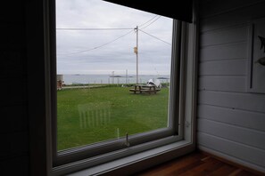 A room with a large window overlooking a grassy area with a picnic table and a utility pole. - Stave Camping (Nordland)