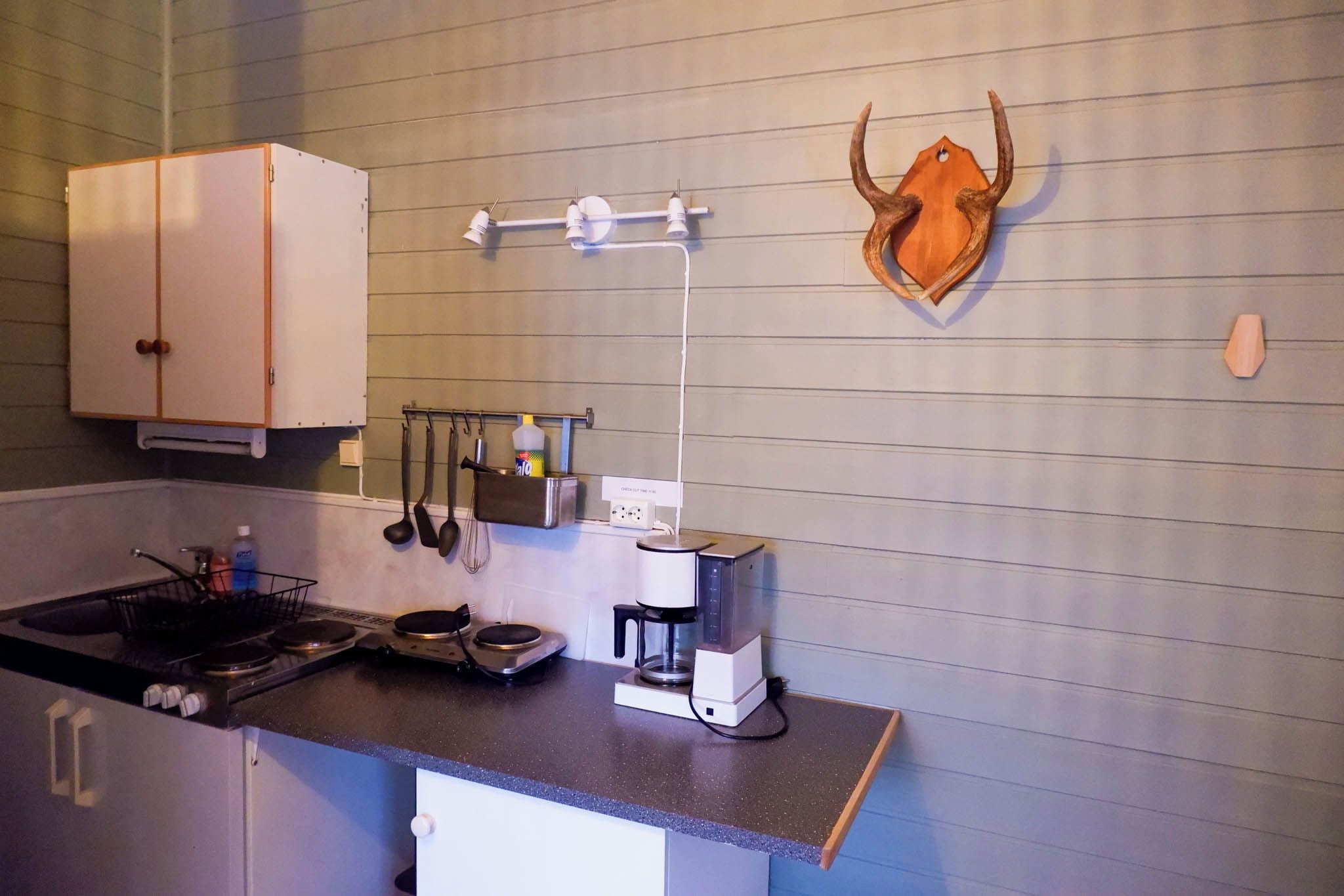 Una cocina compacta con estufa, cafetera y utensilios colgados en la pared.