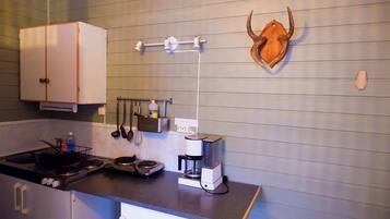 Una cocina compacta con estufa, cafetera y utensilios colgados en la pared.