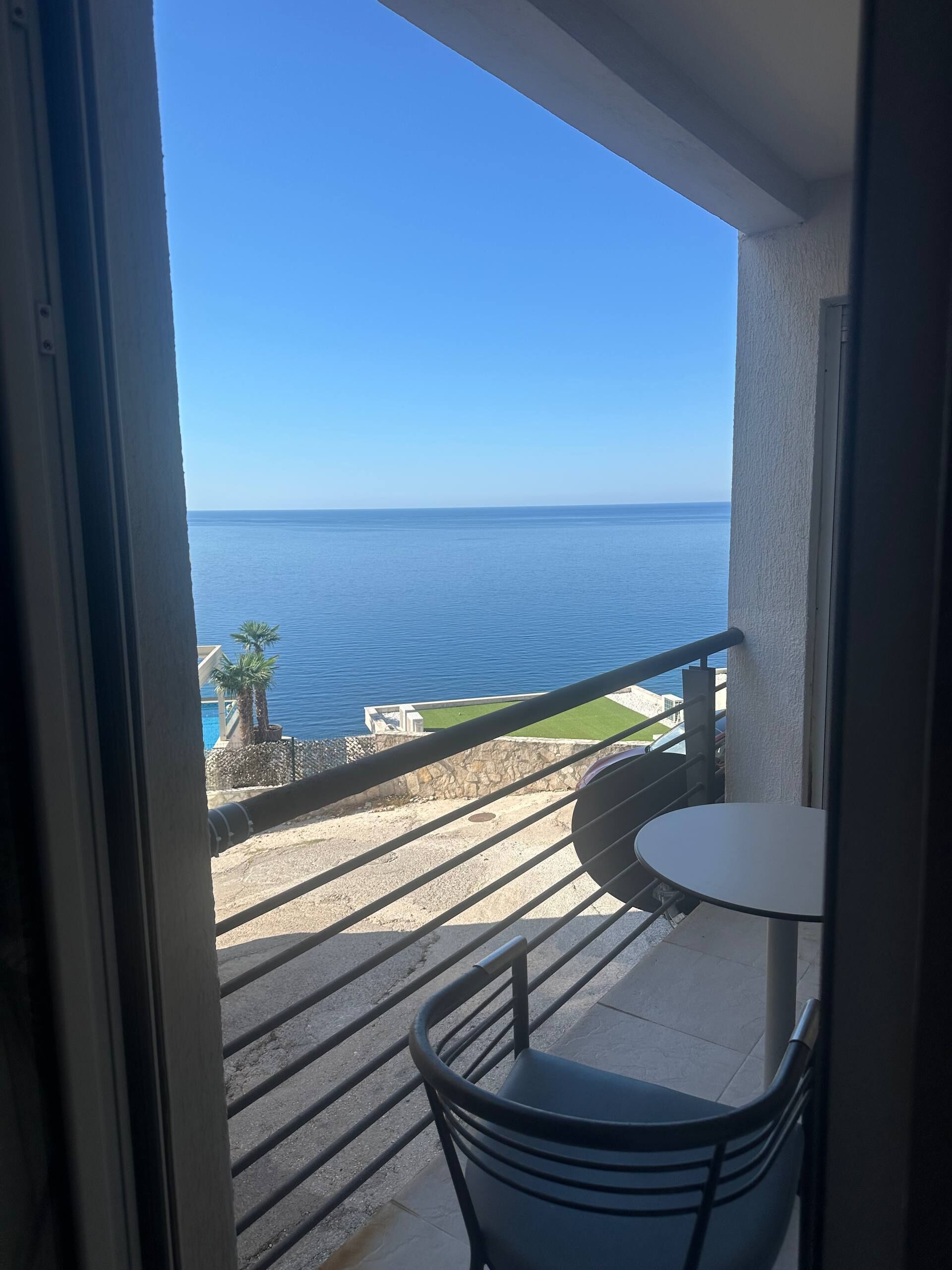 A balcony with a view of the sea, a small table, and a chair.