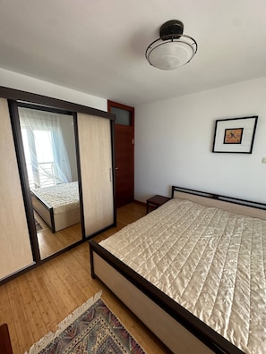 A bedroom with a bed, a mirror, a nightstand, a framed picture on the wall, and a ceiling light fixture. - Aurora Top location views of Old Budva and Adriatic (Budva)