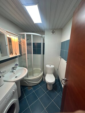 A bathroom with a shower, toilet, sink, and a washing machine. - Aurora Top location views of Old Budva and Adriatic (Budva)