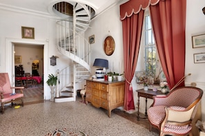 A room with a spiral staircase, a wooden cabinet, a patterned chair, and a dining area with a red tablecloth.