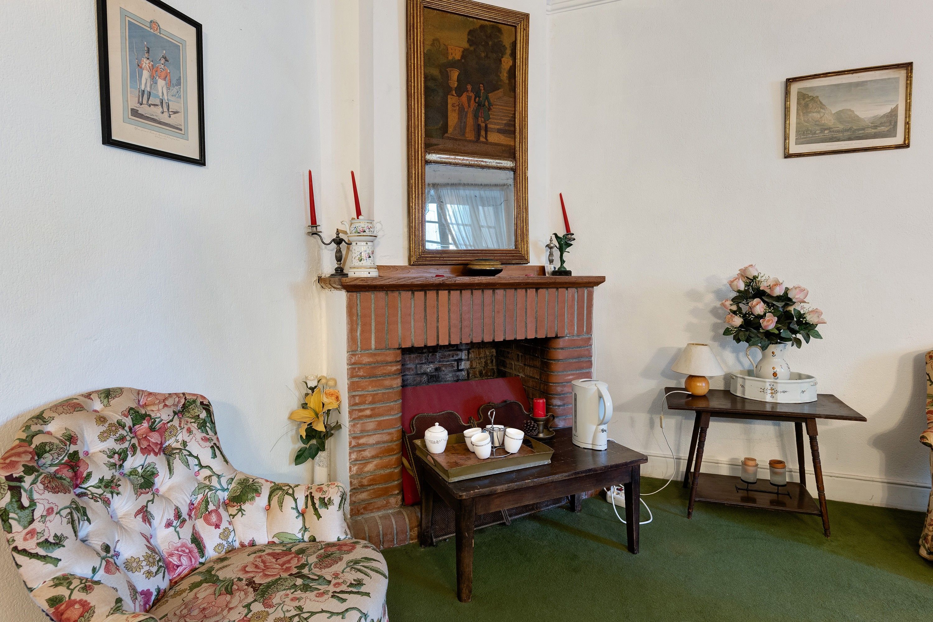 A traditional room with a fireplace, floral armchair, and a table with candles.