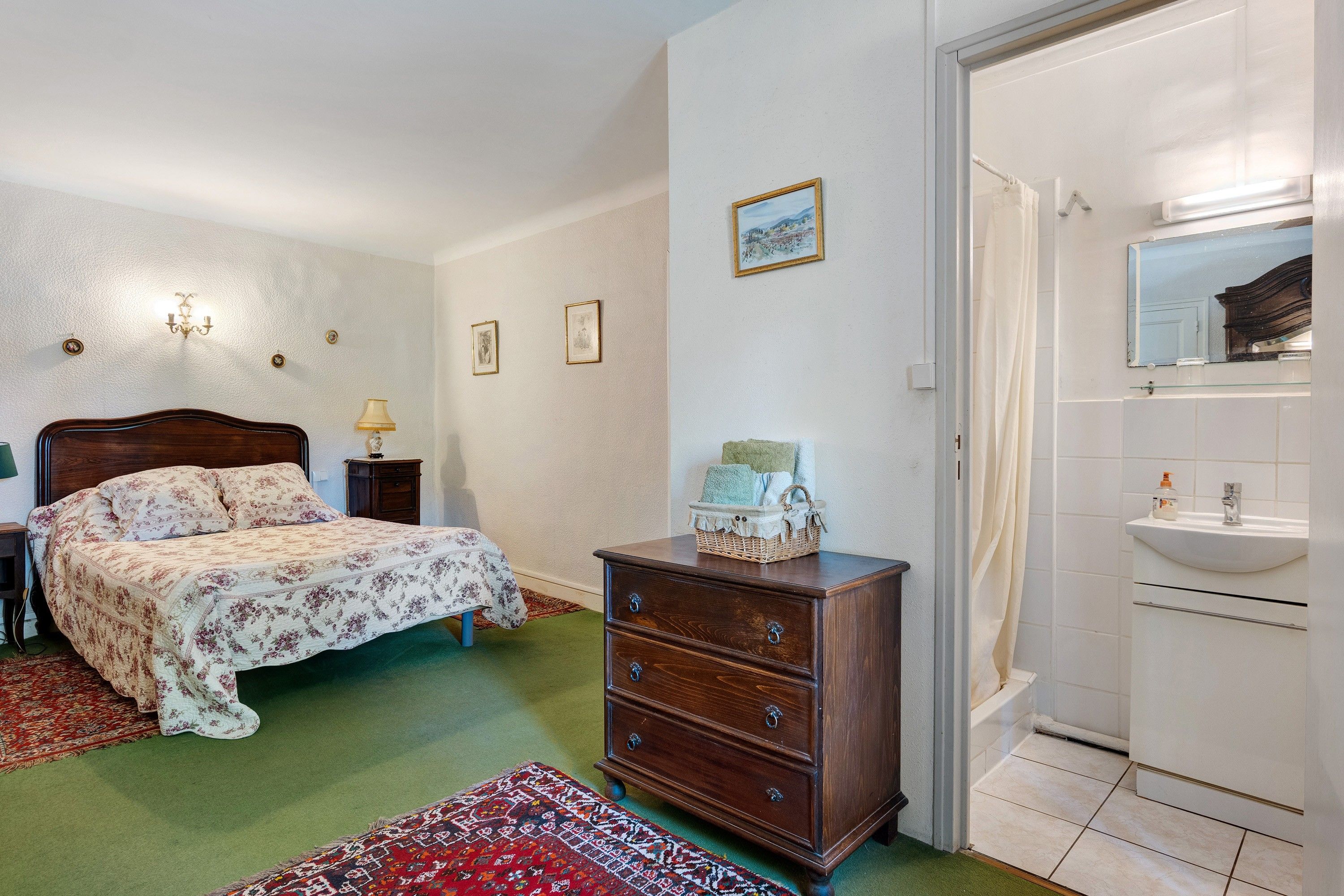 Een slaapkamer met een bed, een dressoir en een badkamer met een wastafel en spiegel.