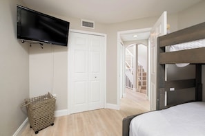 Ein Schlafzimmer mit einem Etagenbett, einem an der Wand montierten Fernseher, einer weißen Tür und einer Treppe, die zu einer weiteren Ebene führt.