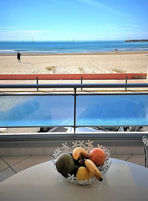 A view of a beach with a person walking, a pier in the distance, and a fruit bowl on a table in the foreground. - Première ligne, t2 cabine pour 4 N123 (Palavas-les-Flots)