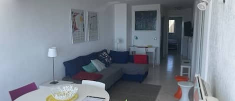 A modern living room with a sofa, a dining table with chairs, and artwork on the walls.