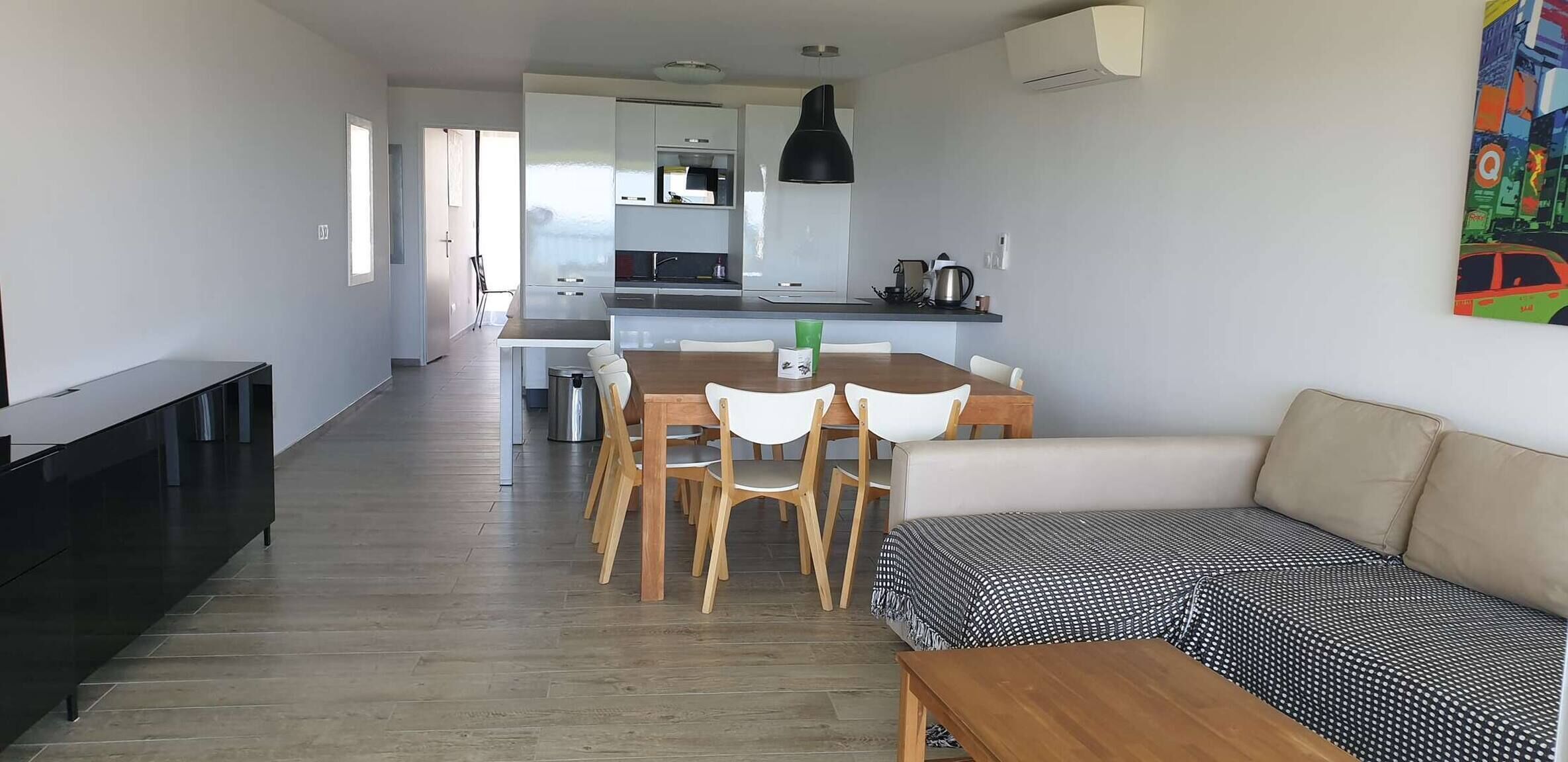 A modern living room with a sofa, a dining table with chairs, a kitchen area with a microwave, and a radiator.