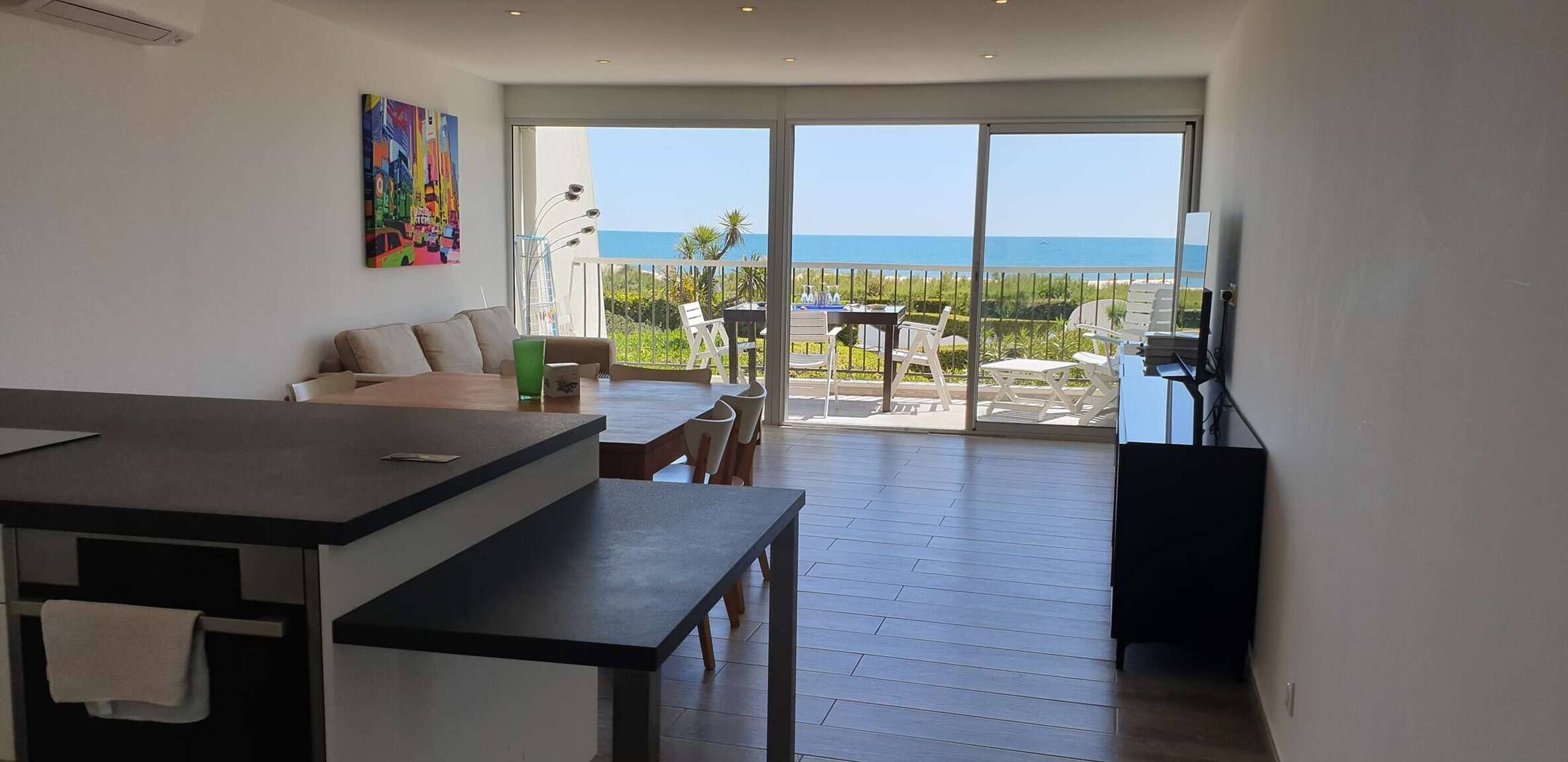 A modern interior with a kitchen area, a dining space, and a balcony with a view of the sea.