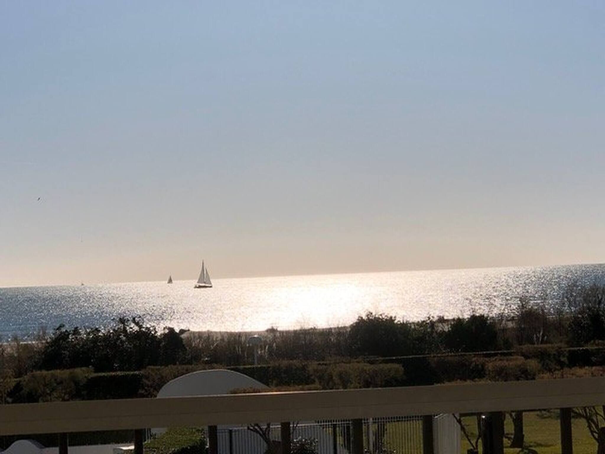 A coastal view with a clear sky, a body of water, and a sailboat in the distance.