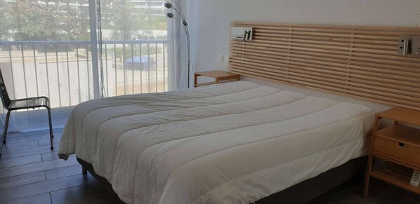 A bedroom with a bed, a chair, a nightstand, and a wooden headboard.