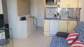 Angolo cottura compatto completo di microonde, macchina del caffè e lavastoviglie. C'è un divano con cuscini decorati e un tavolo in vetro con un telecomando.