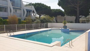 Una piscina rettangolare con bordo piastrellato, circondata da un recinto bianco e alberi.