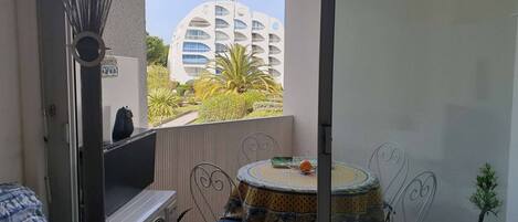 Un balcón con vista a un edificio moderno, una mesa pequeña con una silla y una planta en maceta.