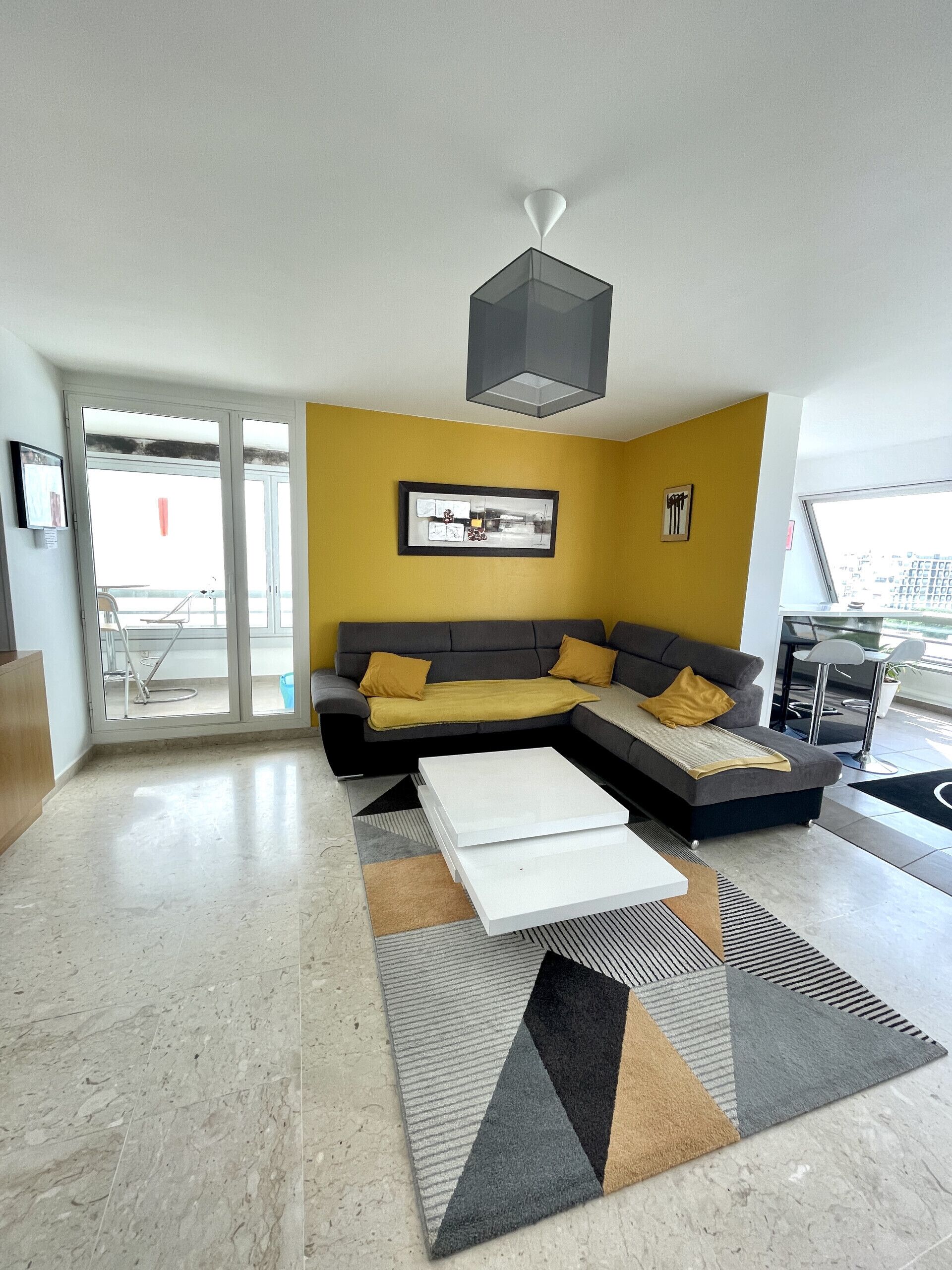 Een moderne woonkamer met een hoekbank, een salontafel en een vloerkleed met een geometrisch patroon.