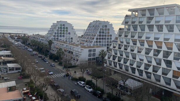 Un edifici modern amb una façana geomètrica singular, a prop d'un carrer amb cotxes i vianants.