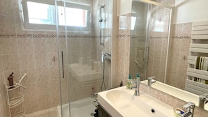 Un bany modern amb plat de dutxa envoltat de vidre, un gran lavabo amb mirall i una barra de tovalloles.