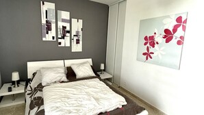 Un dormitori modern amb llit, taules de nit, una obra d'art a la paret i una làmpada al sostre.